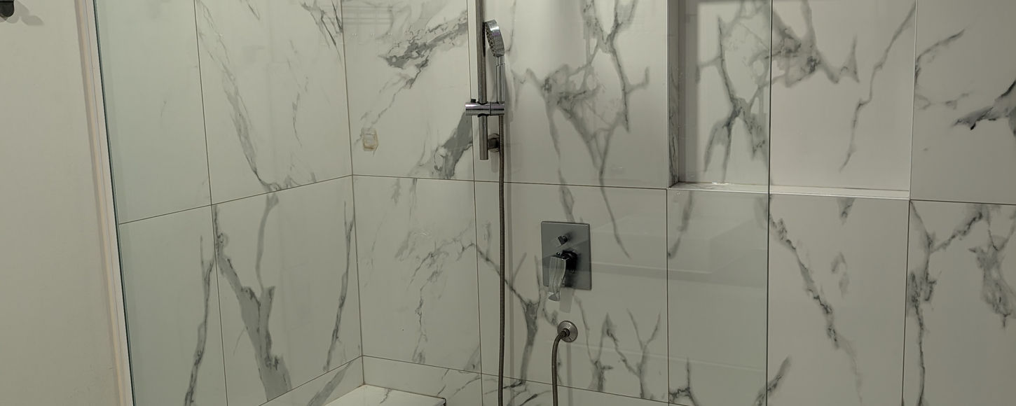 Walk-in shower with glass enclosure and marble-look tile installed in Regina by B-Flex Services with bench and modern bathroom finish.