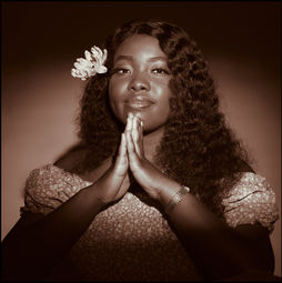 Morolake raises her hands in a spiritual gesture in a warm duotone portrait.