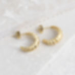 Small gold hoops laying on their side on top of concrete jewellery tray