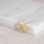 Small gold stud earrings on marble stone