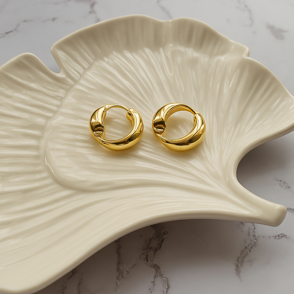 Thumbnail: Elegant gold hoop earrings displayed on a cream leaf shape trinket dish styled on a marble background. Premium jewellery
