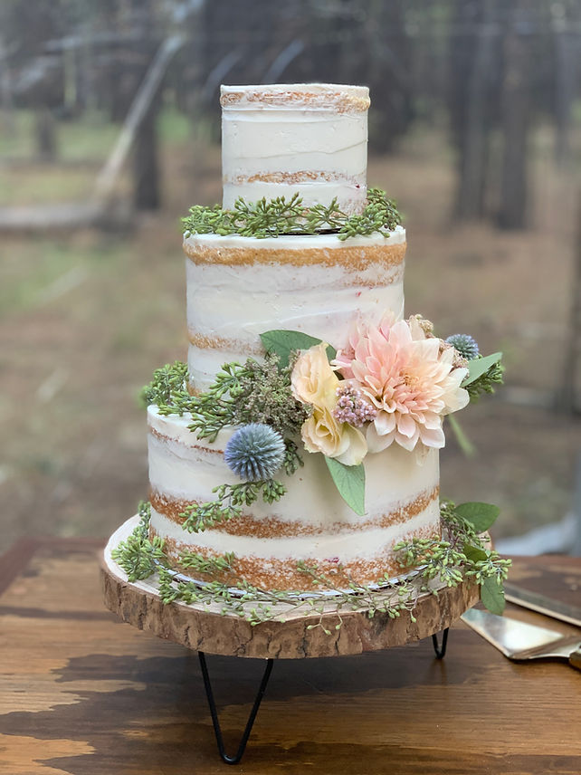 Naked wedding cake decorated with white buttercream and pastel flowers.