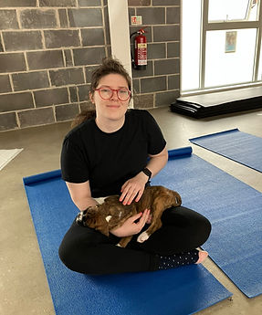 Hannah (Director) with glasses holds puppy on blue yoga mat at gym.