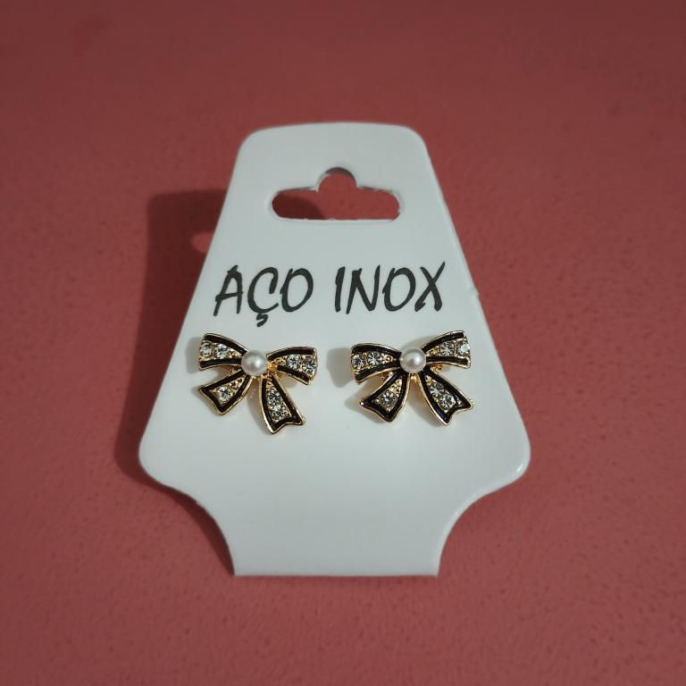 Miniatura: Brinco laço em aço inox dourado com pérola central e strass delicados.