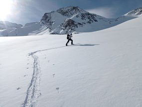 Skieur en randonnée sur une crête enneigée, avançant en autonomie dans un paysage alpin vierge.