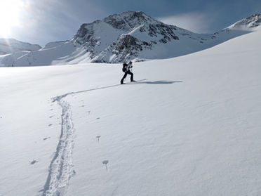 Skieur en randonnée sur une crête enneigée, avançant en autonomie dans un paysage alpin vierge.