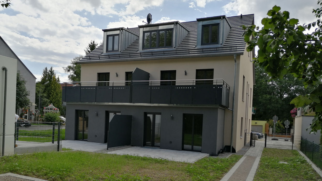Modernes Mehrfamilienhaus mit dunklen Balkonen und Garten.