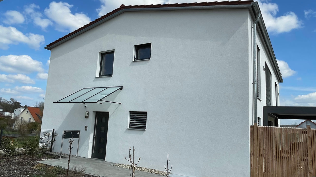 Modernes weißes Wohnhaus mit Glasvordach unter blauem Himmel