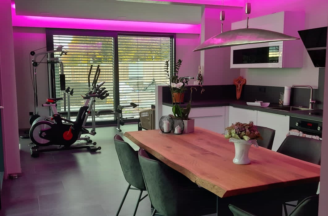Moderner Wohnbereich mit Esstisch und Fitnessgeräten unter pinker LED-Beleuchtung