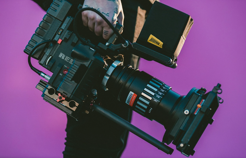A close-up of a man holding a professional production camera against an aesthetic purple background.