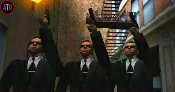 ثلاثة رجال يرتدون بدلات سوداء ونظارات شمسية يرفعون أيديهم بأجهزة في زقاق حضري. يتسمون بالجدية، الخلفية طوب وسلالم خارجية.