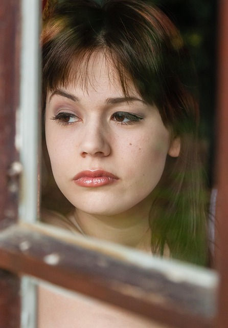 Brunette looking out of a window from the inside with no smile and a blank expression
