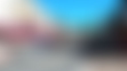 Sunny street with parked cars and colorful buildings. A red awning, shops, and clear blue sky create a vibrant, small-town feel.