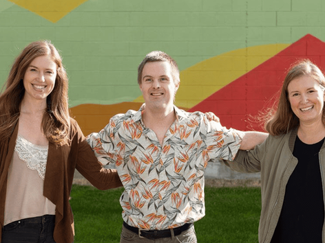 Two female and one male volunteer stand united together smiling.