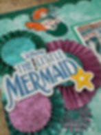 Glittery scrapbook page with "Disney The Little Mermaid" text, features Ariel illustration and sparkly green and purple rosettes.