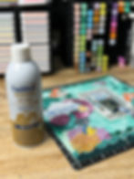 Faultless Premium spray bottle beside a colorful scrapbook page with ocean-themed designs. Background has organized, colorful markers.