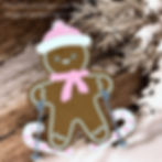 Gingerbread figure in pink hat and scarf skiing with candy cane poles on snow. Background of snowy branches and wood. Text overlays.