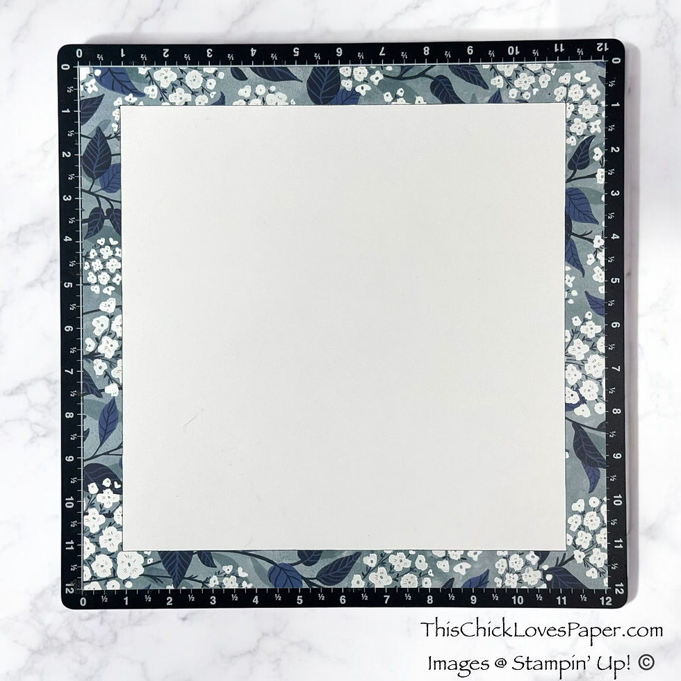 Cutting mat with a floral design border and ruler markings. Blank white square in center. Set on a marble background. Text reads: ThisChickLovesPaper.com.