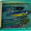 Thumbnail: Sardine can artwork with four engraved fish slightly misaligned, set in resin with blue-green tones by Ortaire de Coupigny