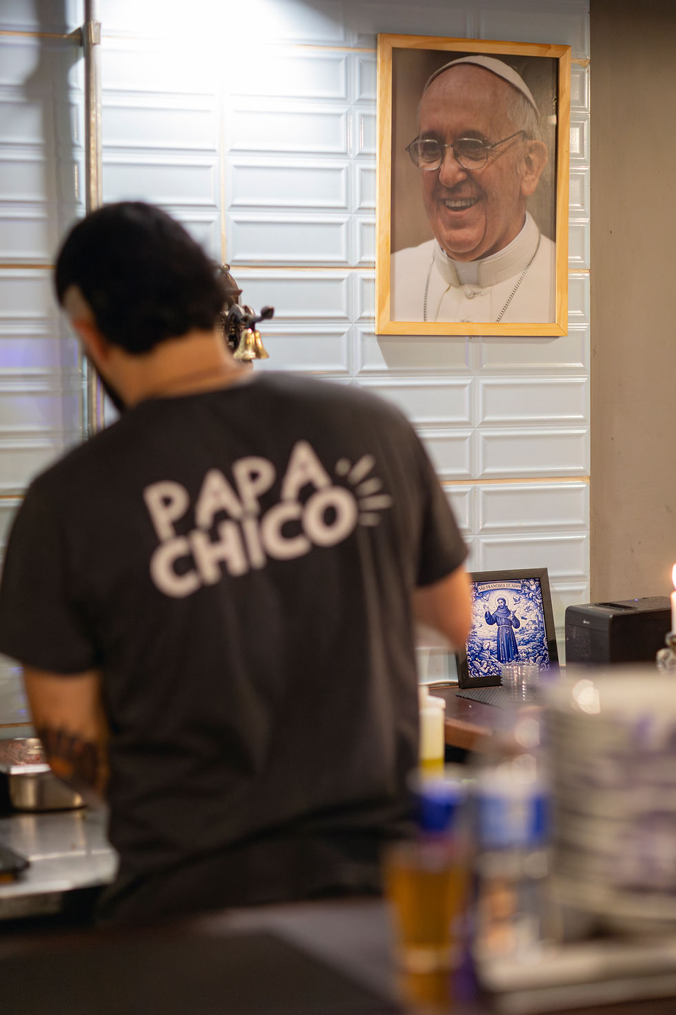 João prepara hambúrguer sob o olhar de uma imagem do Papa Francisco, homenageando o pontífice com o nome da hamburgueria, "Papa Chico". Foto: Eduardo Francischelli.