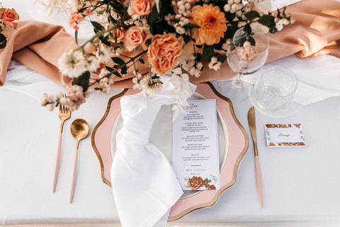 wedding place setting, with pink plates, gold cutlery and floral stationery with pink and peachy roses for the centrepiece arrangements