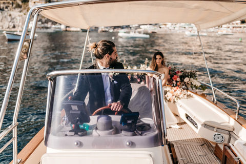 groom looking back at bride while he is driving a boat in the Amalfi coast on their wedding day