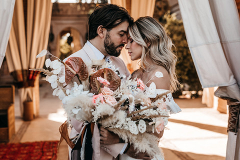 bride and groom with their foreheads together and eyes closed on their elopement wedding day at Beldi Country Club in Marrakech. The bride is holding a bouquet of boho dried flowers and pink roses.