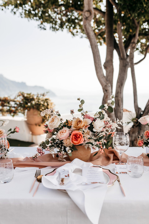 outdoor wedding reception table on the terrace of a Amalfi coast wedding venue. The table is decorated with pink and peach rose floral centrepieces.