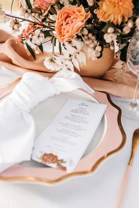 wedding place setting, with pink plates, gold cutlery and floral stationery with pink and peachy roses for the centrepiece arrangements