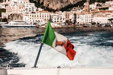 an Italian flag in the wind on the back of a boat in the Amalfi coast