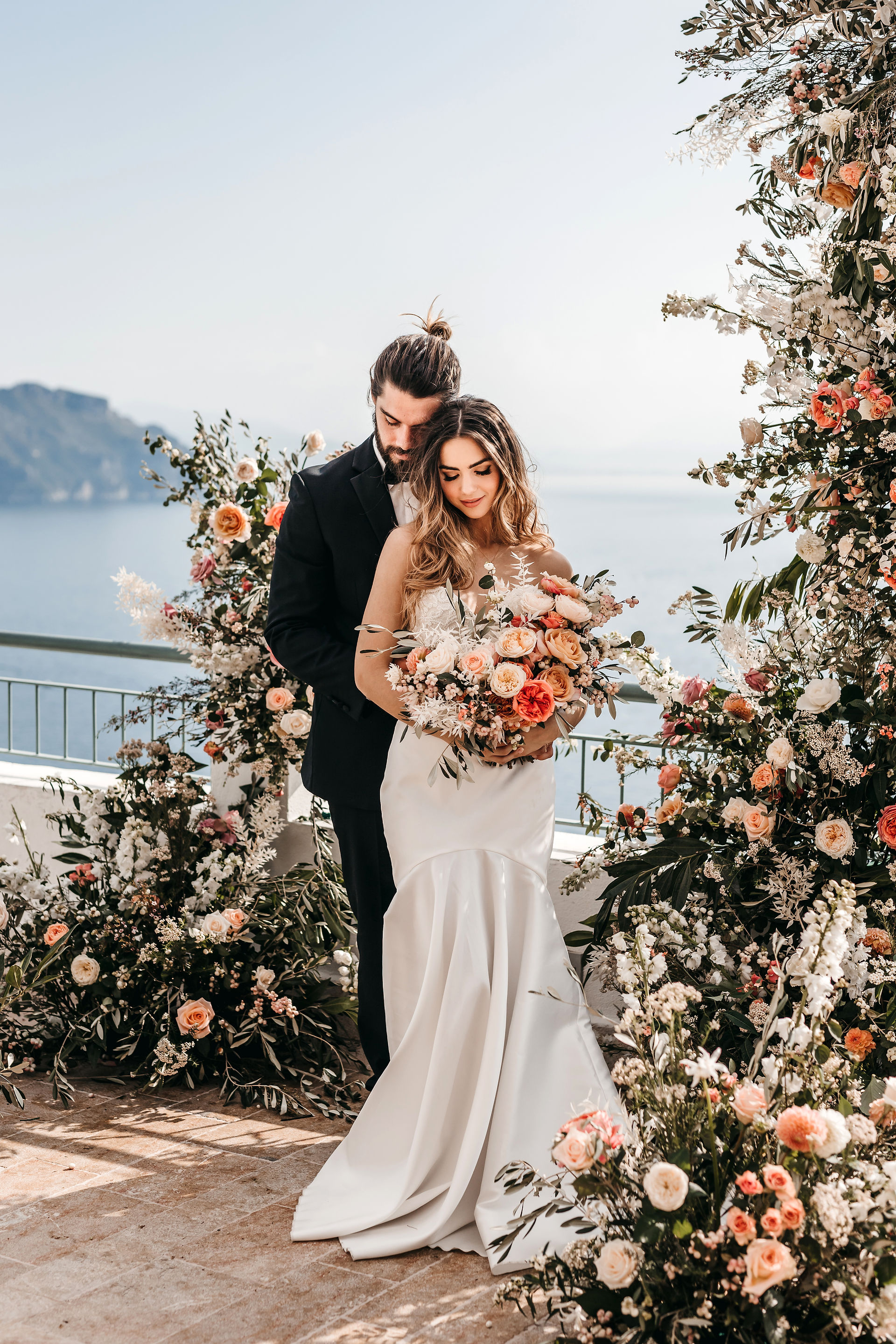 bride and groom standing in front of a floral ceremony set up of pink and white roses on a terrace overlooking the sea on the Amalfi coast for their elopement wedding