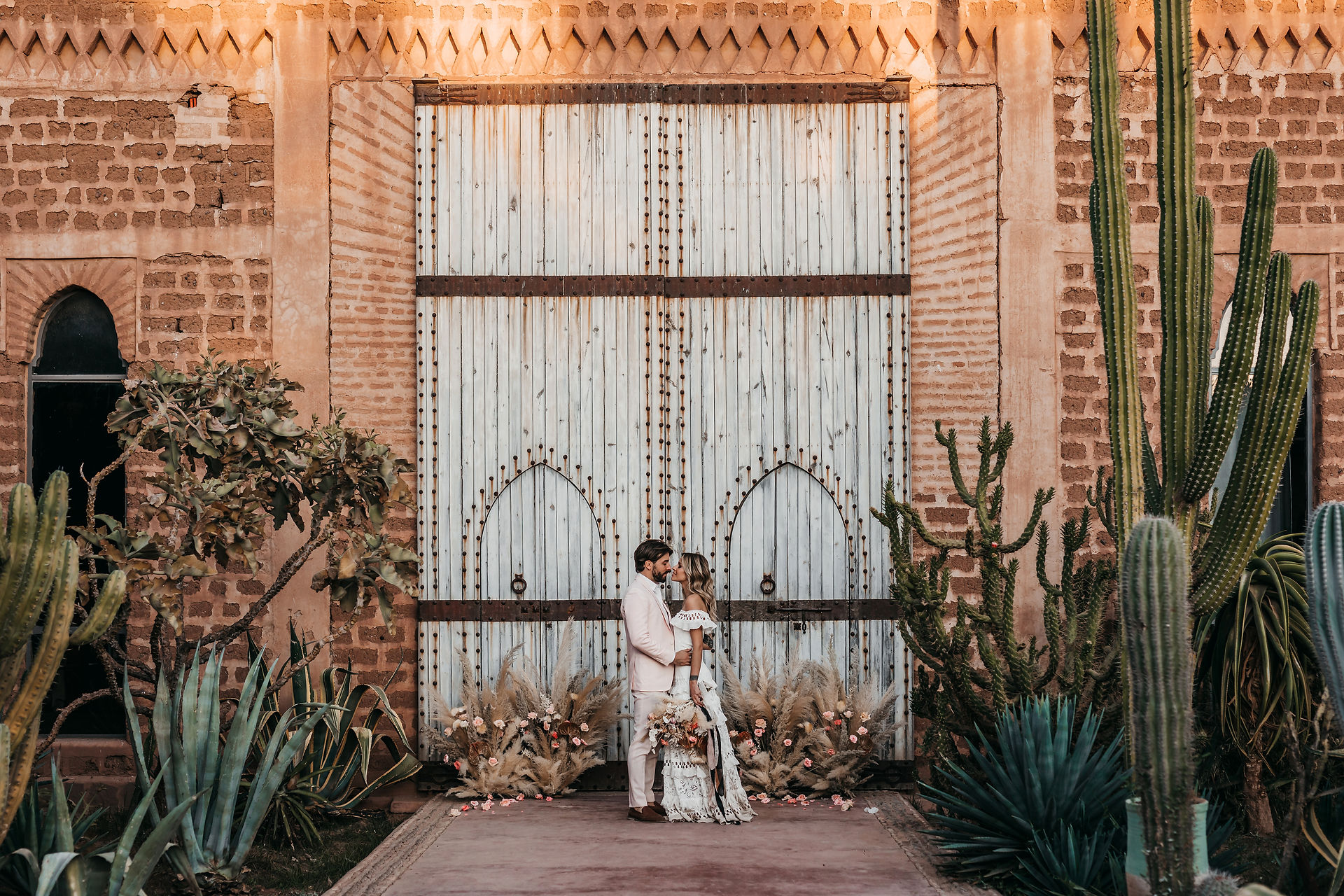 bride and groom standing in front of huge tall doors at Beldi Country Club, they are surrounded by floral arrangements of dried flowers
