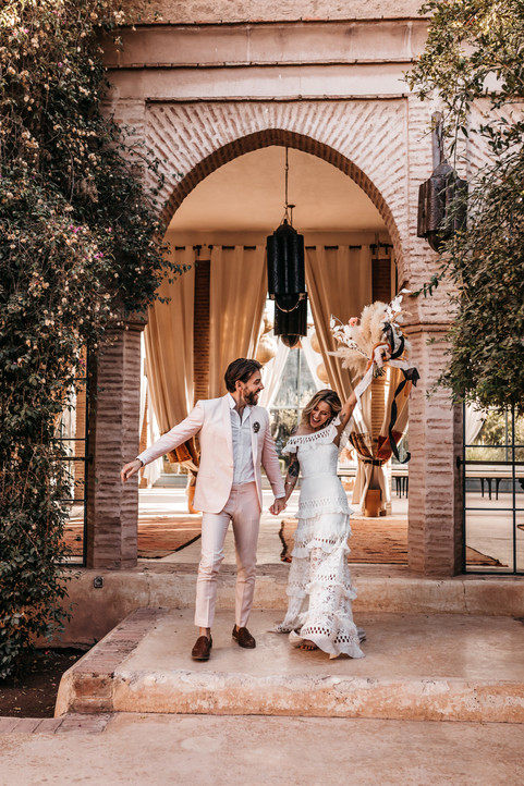 bride and groom holding hands and cheering as they walk together through a moroccan archway at Beldi Country Club a wedding venue in Marrakesh