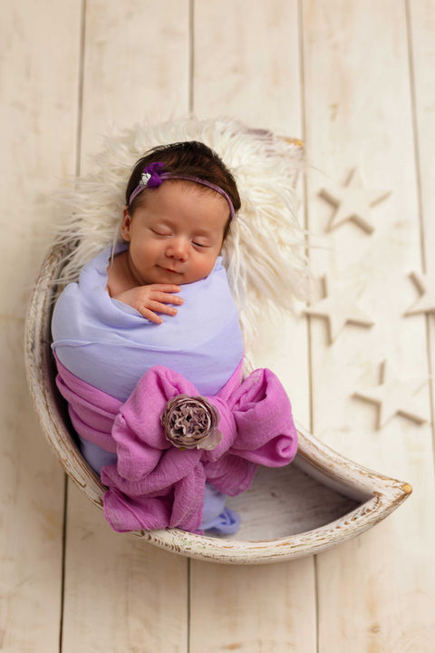 Newborn photoshoot Perthshire – baby wrapped in pastel purple and pink, lying in crescent moon prop