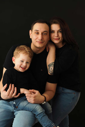 Studio family portrait with parents and their young child photographed on a dark background in Dundee, Scotland.
