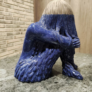 Escultura de mujer abrazada a sus rodillas llorando