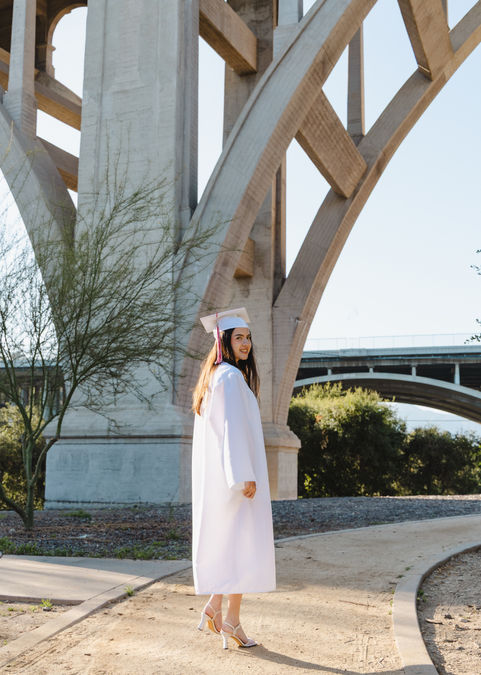 graduate starts to walk away under a bridge