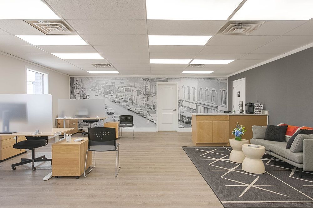 Remodeled office with workstations, a reception counter, lounge seating, and a city mural