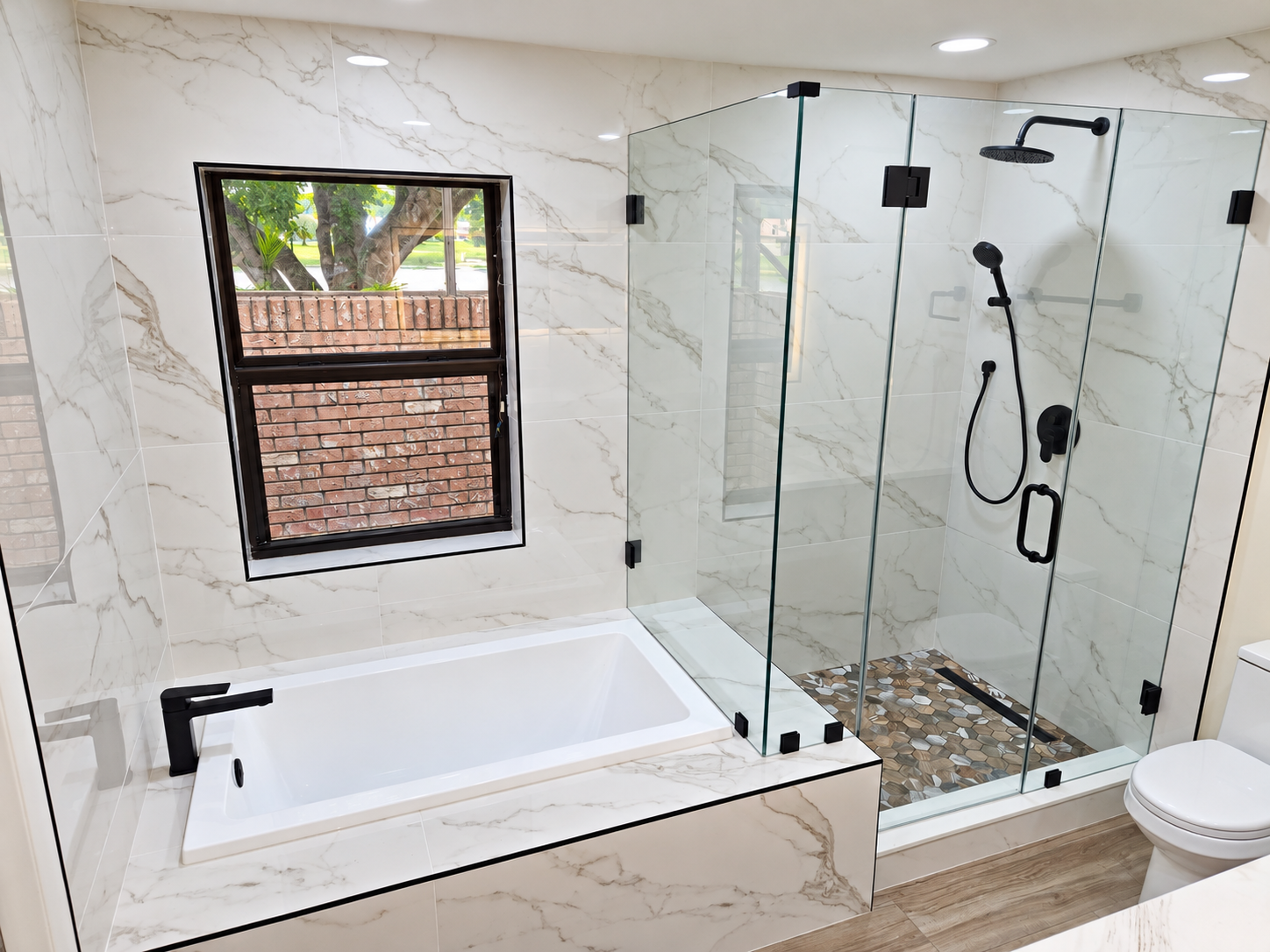 Marble-tiled bathroom with a bathtub, glass shower, and black fixtures