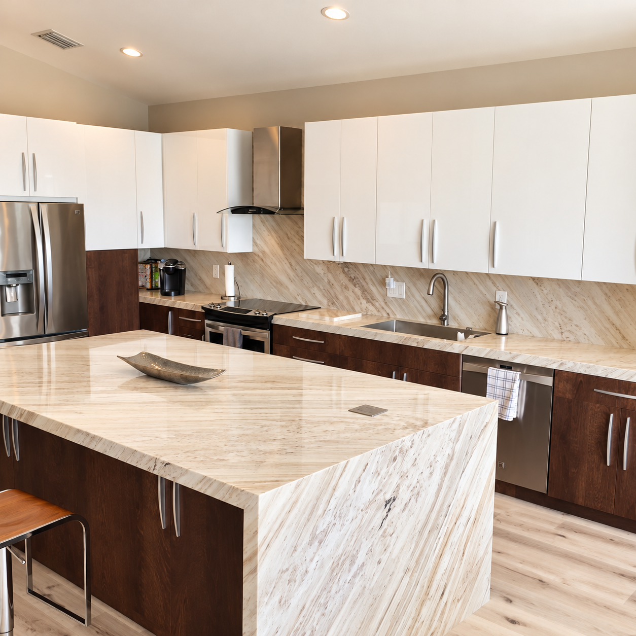 Kitchen with white upper cabinets, dark wood lower cabinets, stainless appliances, and a marble waterfall island