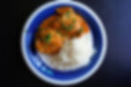A blue and white plate with chicken curry garnished with herbs, and a serving of white rice on a dark table.