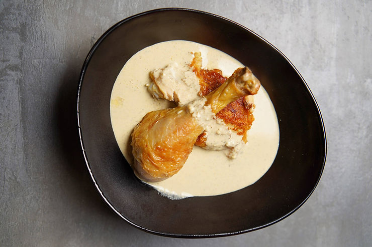 Roasted chicken leg in creamy sauce on a black plate, shot from above on a gray background. Chicken Bazhe