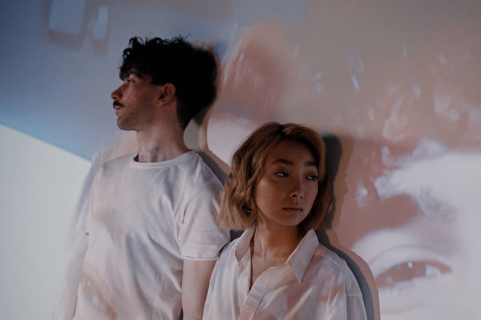 A couple stand side by side against a wall, each looking in a different direction.