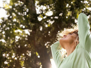 Woman smiling and looking towards the sun, embodying a sense of wellbeing