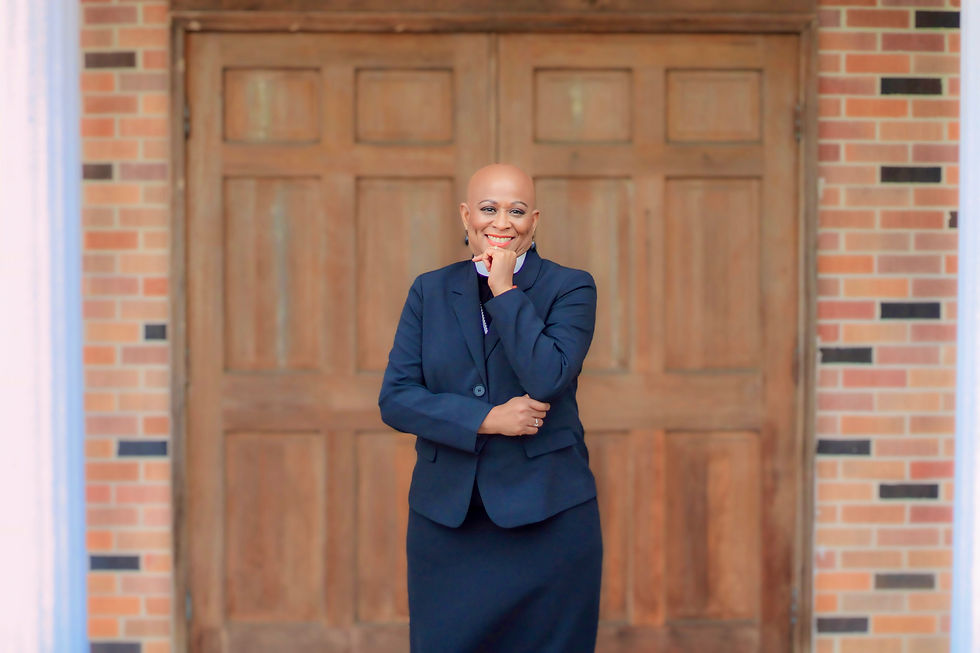 Sherri L. Jackson smiling and posing in a black suit in front of wooden doors.