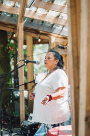 Rosemary Georgeson speaks into a microphone at an outdoor venue with wooden posts and a string of lights