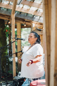 Rosemary Georgeson speaks into a microphone at an outdoor venue with wooden posts and a string of lights
