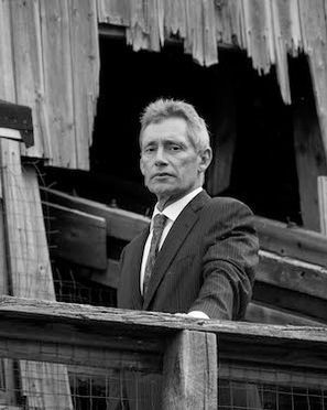 Martin West in a suit and tie stands in a dilapidated wooden structure