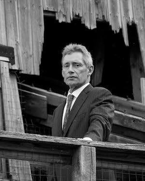 Martin West in a suit and tie stands in a dilapidated wooden structure