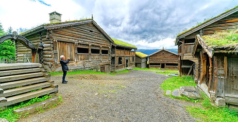 Maihaugen med hytter og grønt landskap, og en person som tar bilde